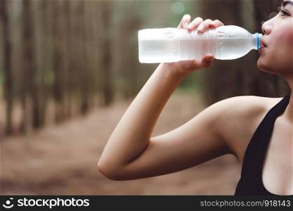 Close up of Beauty Asian woman drinking purify water by right hand after exercise in forest. Thirsty girl in black sport wear. Workout and Sports concept. People and Outdoor Nature theme.