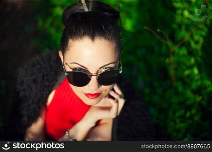 Close-up of beauty girl in trendy sunglasses in the spring park. Green background.. Close-up of beauty girl in trendy sunglasses in the spring park.