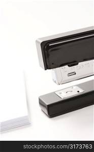 Close up of black stapler on white background with stack of paper.