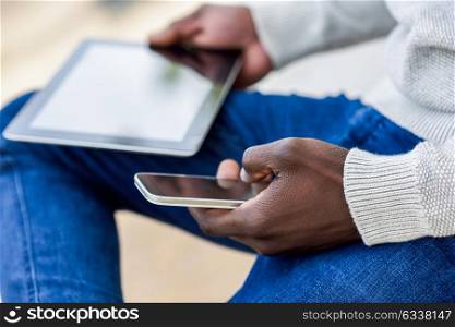 Close-up of black young man hands holding tablet computer and smartphone in urban background.