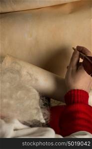 Close-up of blank Christmas letter on old paper roll in Santa Claus hands with quill pen