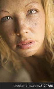 Close-up of blond womans muddy face looking at viewer.