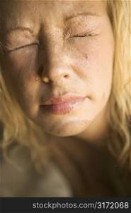 Close-up of blond womans muddy face with closed squinting eyes.