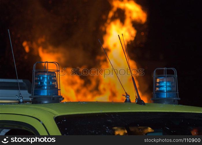 Close-up of Blue Siren on Emergency Vehicle and Fire in background. Detail of Flashing Blue Siren Light on Roof of Emergency Vehicle