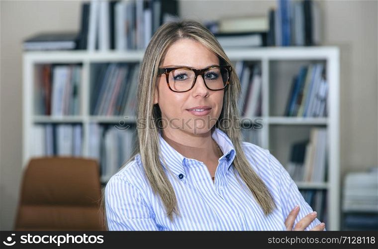 Close up of bonde smiling businesswoman standing in office against of bookcase. Close up of blonde smiling businesswoman in office