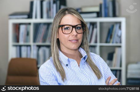 Close up of bonde smiling businesswoman standing in office against of bookcase. Close up of blonde smiling businesswoman in office