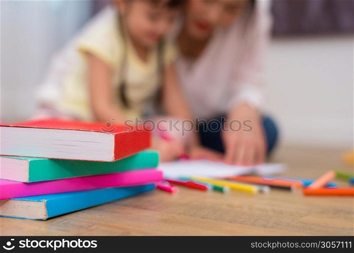 Close up of books and crayon color on floor with mom and kids background. Back to school and Art education learning concept. Children and teacher theme.. Close up of books on floor with mom and kids background. Back to school and Education concept. Children and teacher theme.