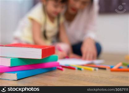 Close up of books and crayon color on floor with mom and kids background. Back to school and Art education learning concept. Children and teacher theme.. Close up of books on floor with mom and kids background. Back to school and Education concept. Children and teacher theme.