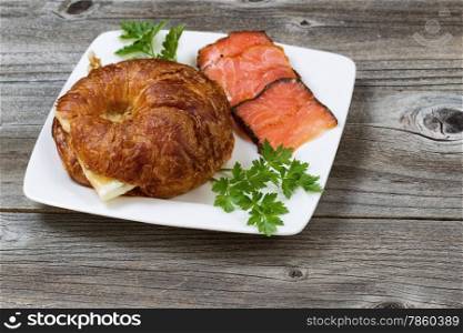 Close up of breakfast including freshly baked croissant, with egg, cold smoked salmon and parsley on side on rustic wooden boards.