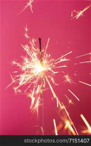 Close up of Brightly burning sparkler on a pink background with lots of sparks. Happy New Year concept. Close up of Brightly burning sparkler on a pink background.