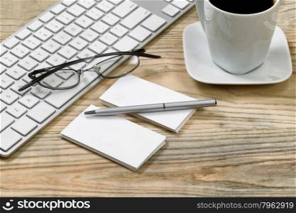 Close up of business cards and silver pen. Computer keyboard, reading glasses and cup of coffee in background on desktop.
