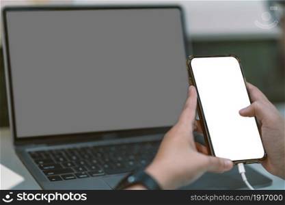 Close-up of business female wearing smartwatch working with and hand holding of smartphone with empty white screen and laptop in coffee shop like the background.