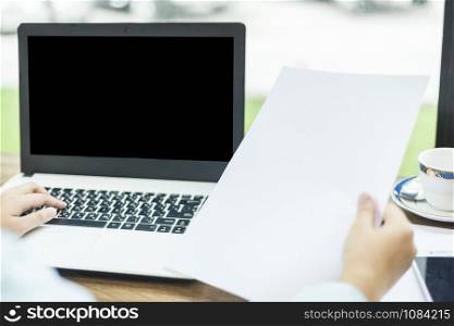 Close-up of business female working with laptop and Hand holding of blank white document in coffee shop like the background.