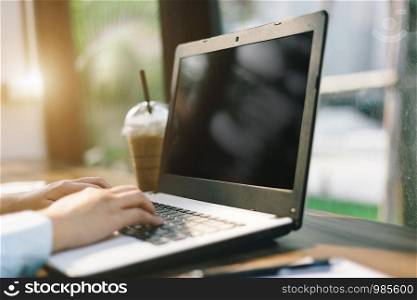 Close-up of business female working with laptop with blank white screen make a note document and smartphone in coffee shop like the background.