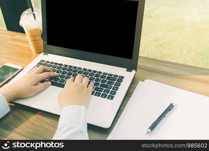 Close-up of business female working with laptop with blank white screen make a note document and smartphone in coffee shop like the background.