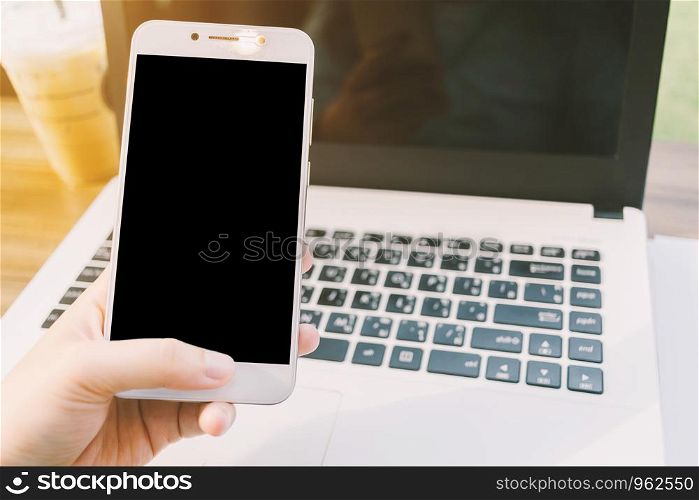 Close-up of business female working with smartphone with blank black screen make a note document and laptop in coffee shop like.