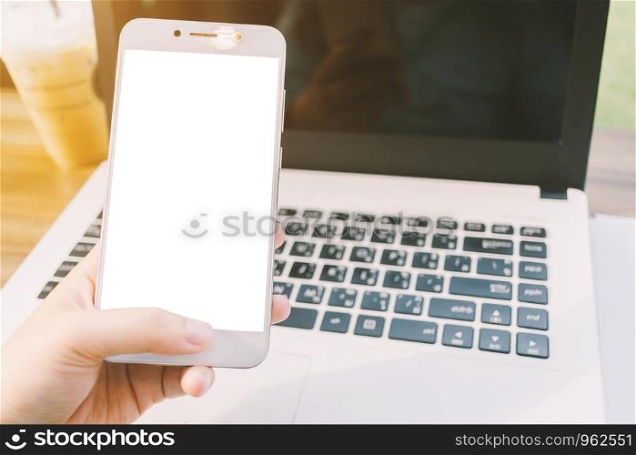 Close-up of business female working with smartphone with blank white screen make a note document and laptop in coffee shop like.