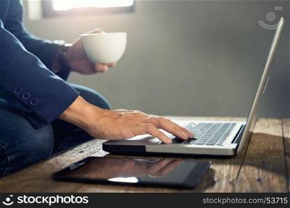 Close up of Business man hands busy working on his laptop and drinking hot coffee andsitting at wooden table in a coffee shop.