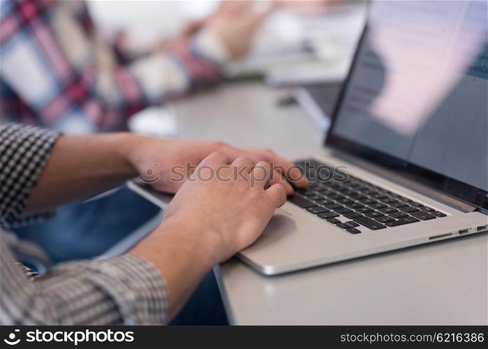 close up of business man hands typing on laptop computer at modern startup office, blured team in meeting, people group in background