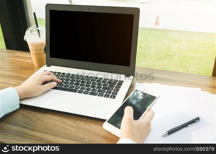 Close-up of Business woman working with smartphone,laptop with blank black screen and document in coffee shop like the background.