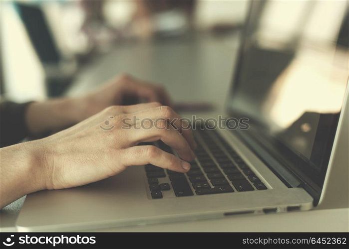 close up of business womans hand typing on laptop at modern startup office computer, blured team in meeting, people group in background