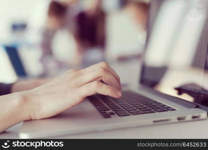 close up of business womans hand typing on laptop at modern startup office computer, blured team in meeting, people group in background