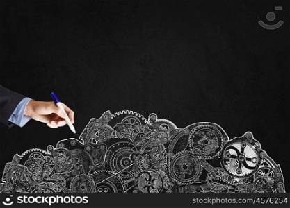 Close up of businessman hand drawing gears on black wall. Businessman drawing cogwheels