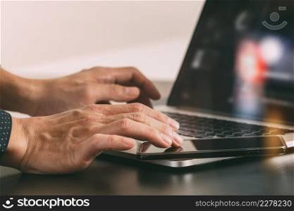 close up of businessman hand working with smart phone and laptop and digital tablet computer in modern office with glass reflected view