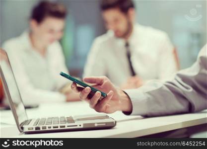 close up of businessman hands using smart phone and laptop computer, people group in office meeting room blurred in backgronud