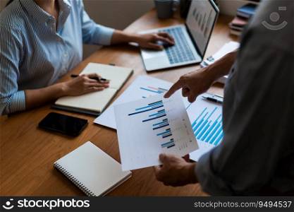 Close up of businessman pointing on chart of financial document and businesswoman typing on laptop.
