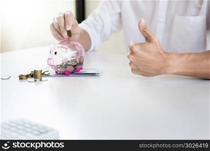 Close up of Businessman putting coin into small piggy bank , The concept of saving money and investment.. Close up of Businessman putting coin into small piggy bank , The