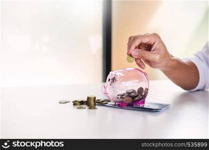 Close up of Businessman putting coin into small piggy bank , The concept of saving money and investment.
