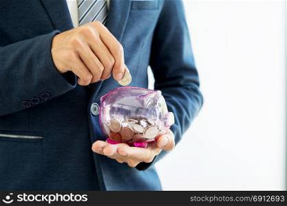 Close up of Businessman putting coin into small piggy bank , The concept of saving money and investment