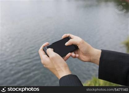 Close-up of businessman&rsquo;s hands texting on smart phone along river