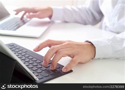 close up of businessman typing keyboard with laptop computer and digital tablet on white desk in modern office