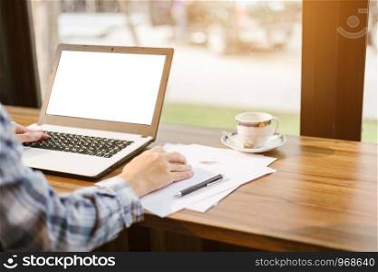 Close-up of businessman working with laptop with blank white screen,smart phone and document on in coffee shop like the background.