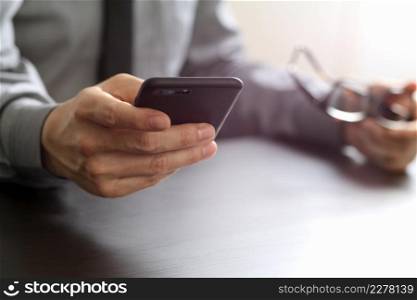 close up of businessman working with mobile phone and eyeglass on wooden desk in modern office