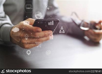 close up of businessman working with mobile phone and eyeglass on wooden desk in modern office with virtual reality icon diagram 