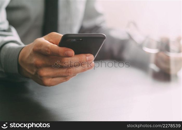 close up of businessman working with mobile phone and eyeglass on wooden desk in modern office