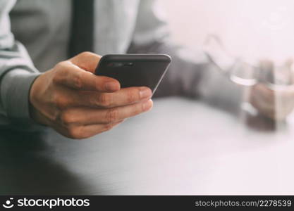 close up of businessman working with mobile phone and eyeglass on wooden desk in modern office