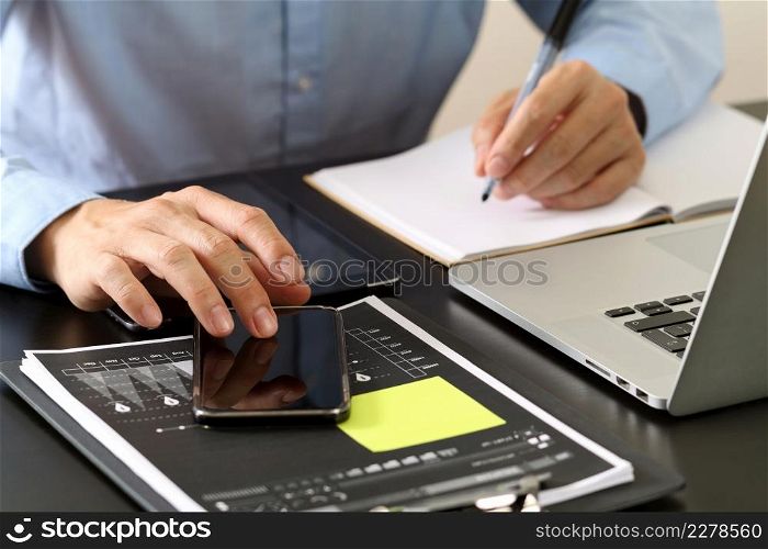 close up of businessman working with smart phone and digital tablet and laptop computer on wooden desk in modern office