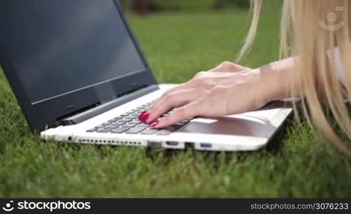 Close up of businesswoman hands typing on a laptop in the park on green lawn. Side view of female hands working with a laptop outdoor.