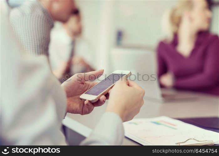close up of businesswoman hands using smart phone, people group in office meeting room blurred in backgronud