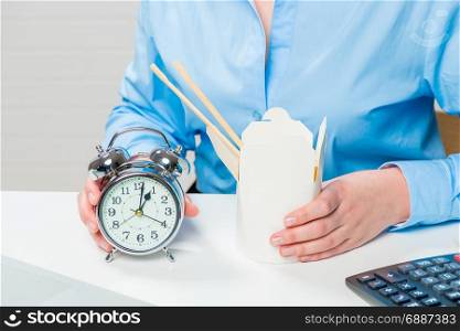 Close-up of businesswoman&rsquo;s hands with an alarm clock and noodles in a box