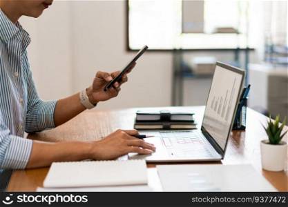 Close up of businesswoman searching business data on smartphone while working on laptop in office.