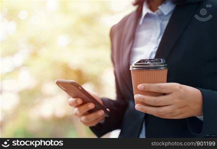 Close up of businesswoman using smartphone and drinking hot coffee in the morning, business and lifestyle concept