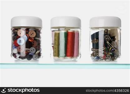 Close-up of buttons and safety pins with thread spools in three different jars