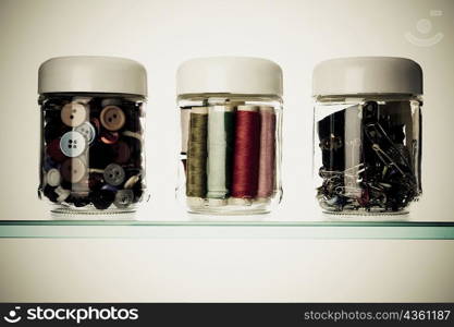 Close-up of buttons and safety pins with thread spools in three different jars