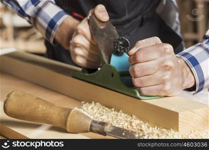 Close up of carpenter hands working with plane in his studio