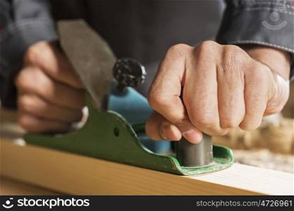 Close up of carpenter hands working with plane in his studio